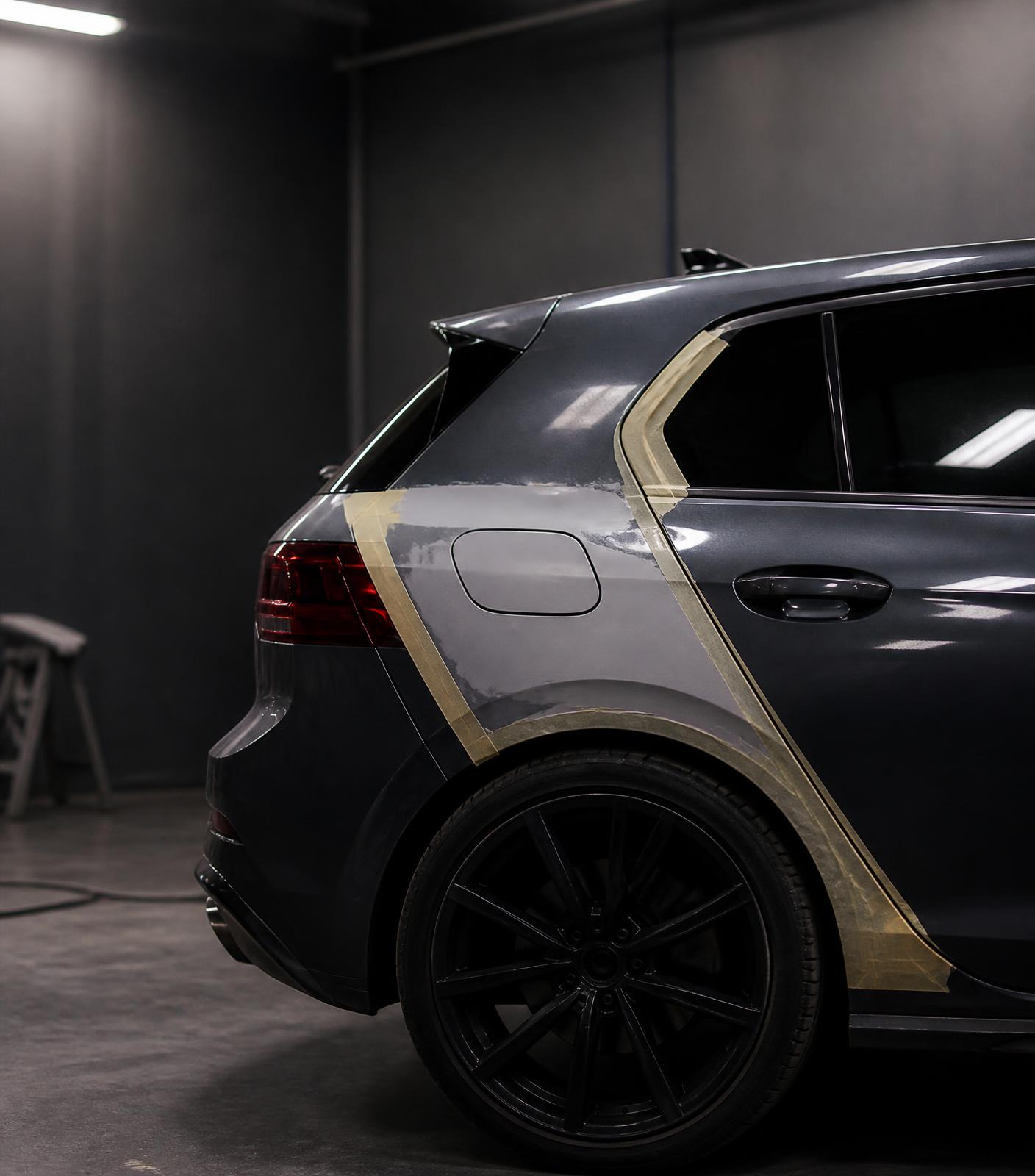 Vehicle rear quarter panel masked and prepared for bodywork repair in a workshop