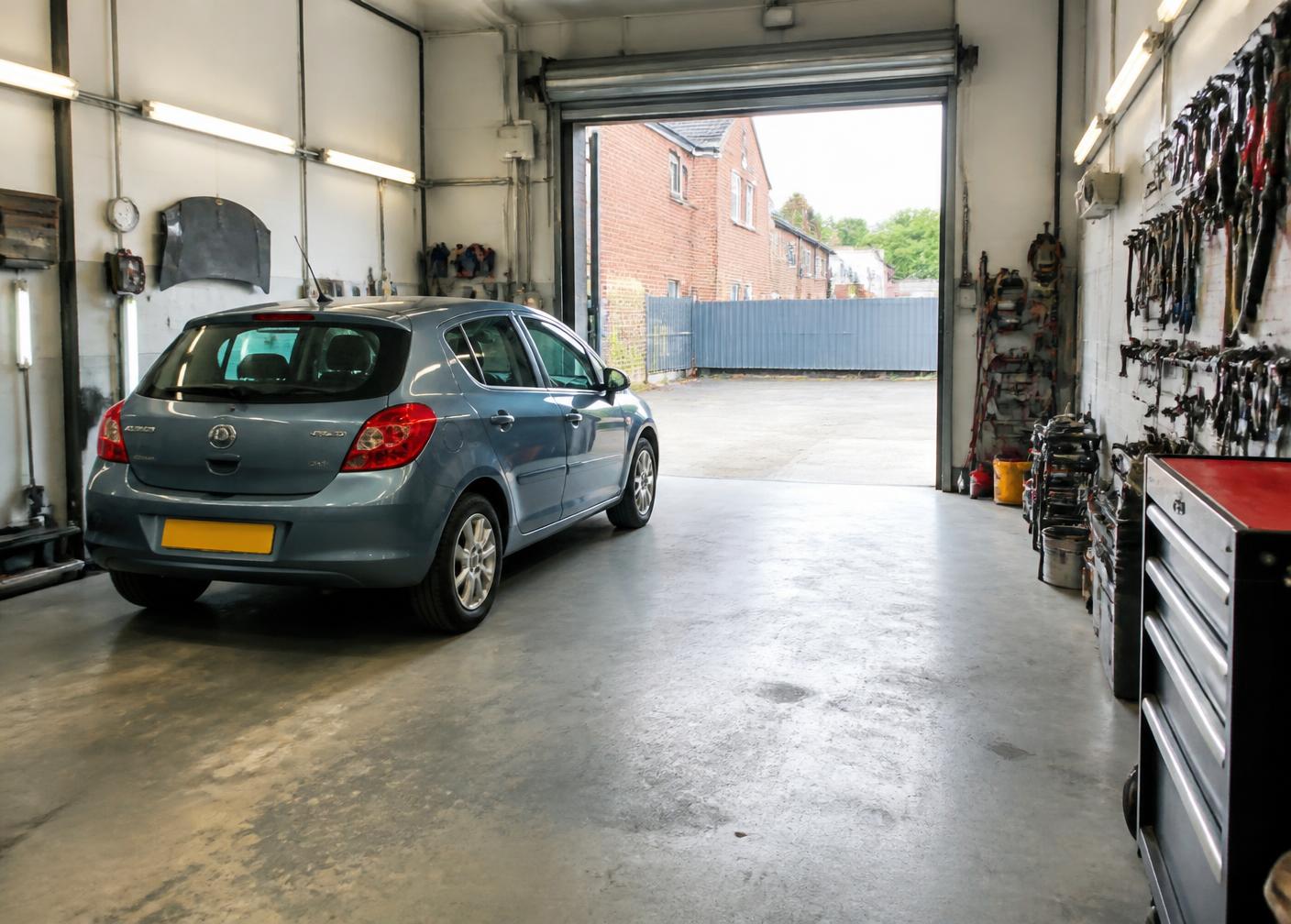 Interior of a tidy independent vehicle repair workshop with a car parked by the open shutter door